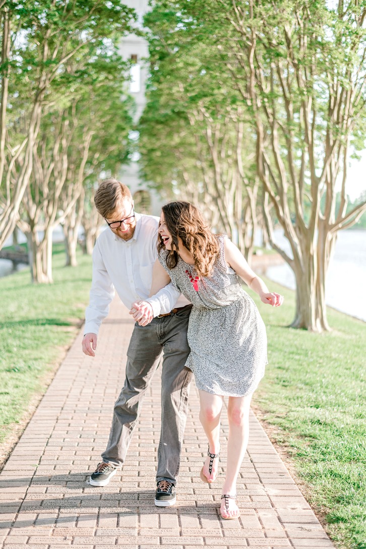 fiancés walk down a cobblestone sidewalk by a river holding hands and laughing during Furman University engagement session