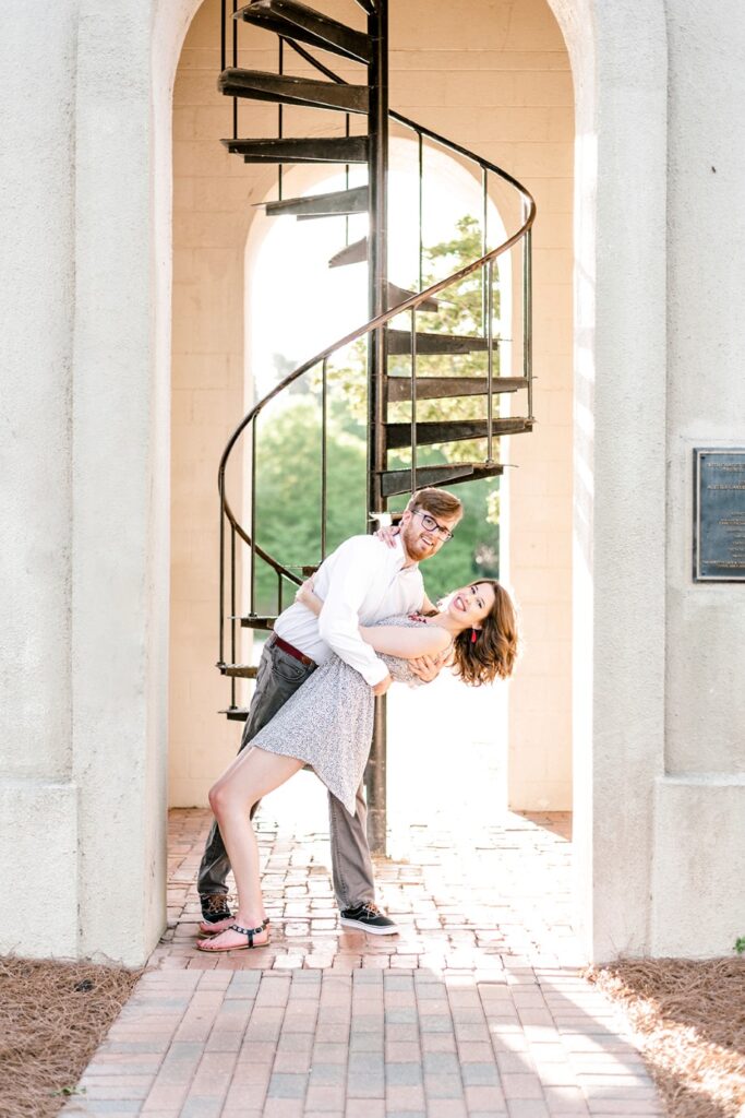 fiance dips his future bride with a spiral stair case in the background during Furman University engagement session
