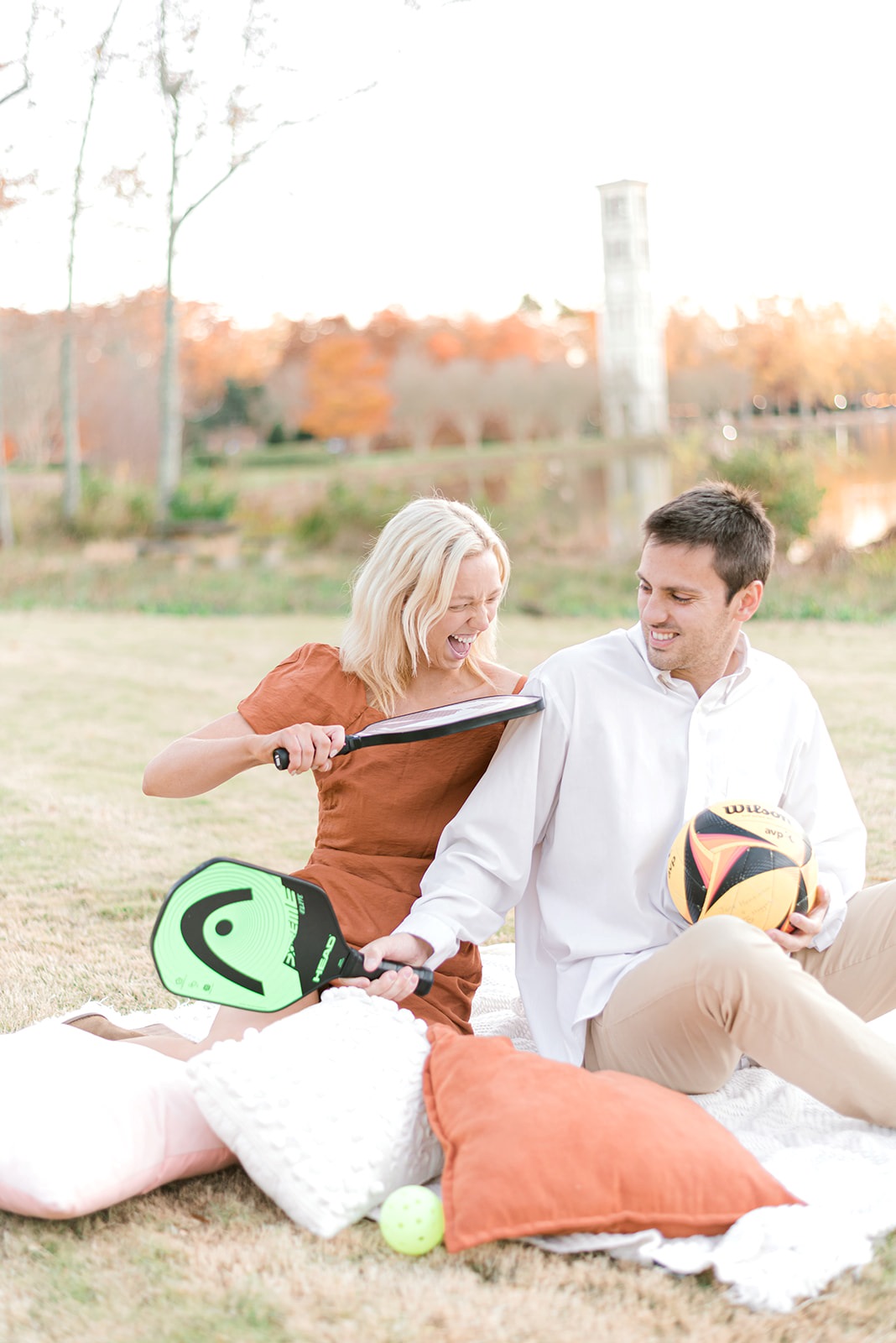 Furman University engagement photos by Greenville engagement photographer. Woman with short blonde hair flirts with fiancé touching him with a tennis racket.