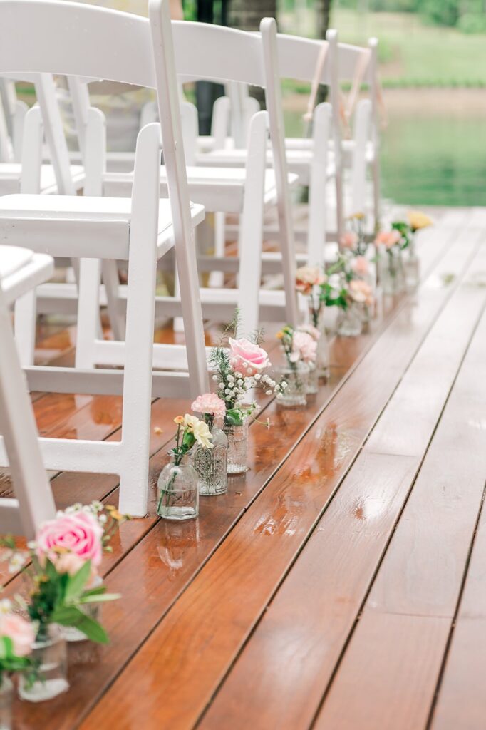 white chairs line a wooden floor with flowers in jars at a Piney Grove Ranch wedding