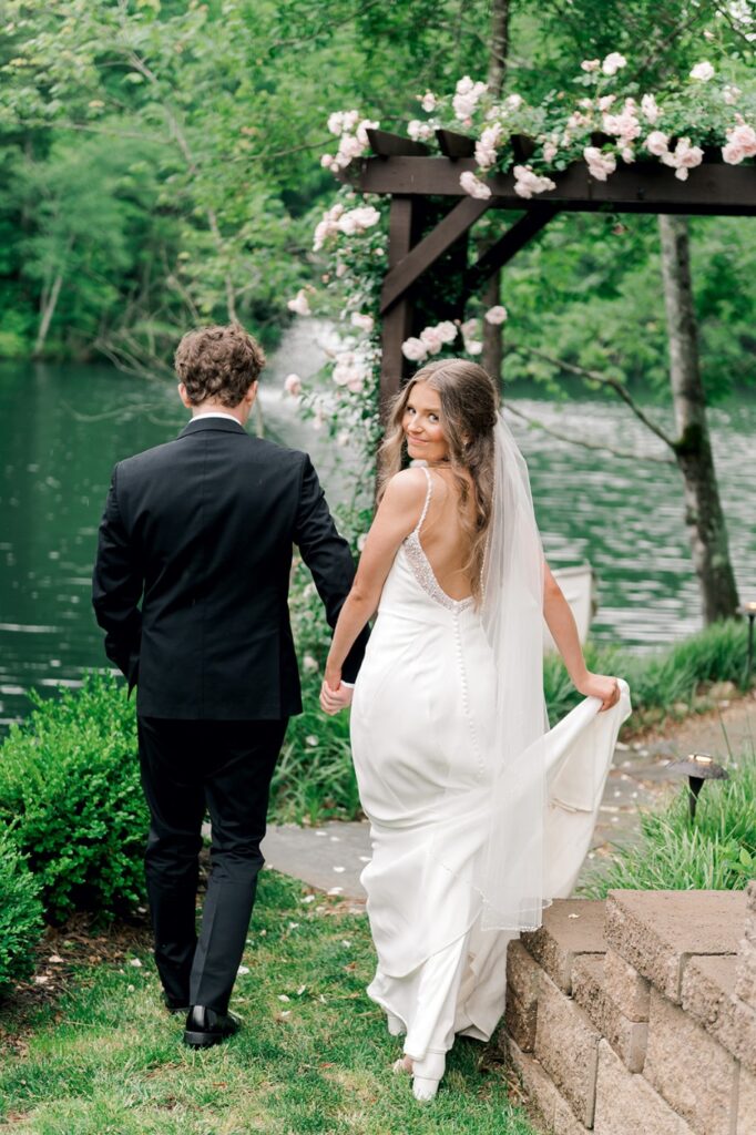 bride looks back at camera as they walk towards wedding arch during bridal photos at piney grove ranch wedding