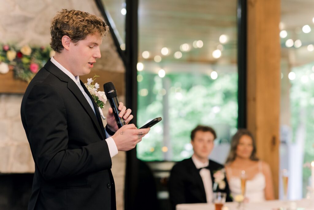 man makes speech holding a phone and microphone at Piney Grove Ranch wedding
