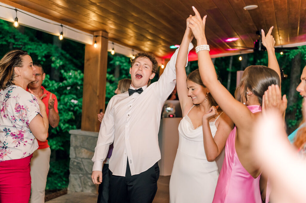 Groom and bride hold hands and put it in the air in celebration while the bride smiles and groom yells in celebration at piney grove ranch wedding