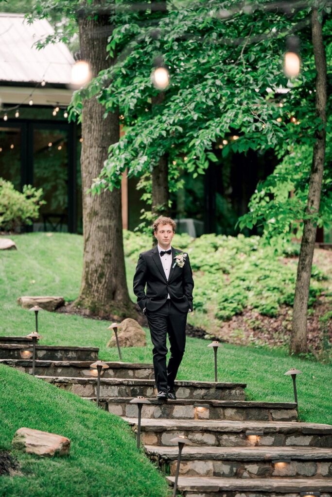 Man walks down stone stairs to Piney Grove Ranch wedding ceremony. Beautiful trees and string lights line the path. 