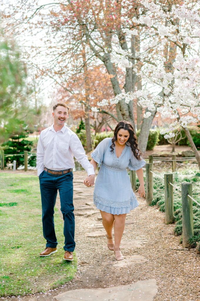 Couple walking hand in hand wearing formal dress under cherry blossom trees at Furman University in Greenville SC