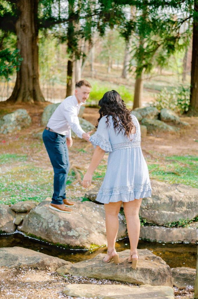 Male assists female wearing blue dress crossing the creek at Furman University in Greenville SC