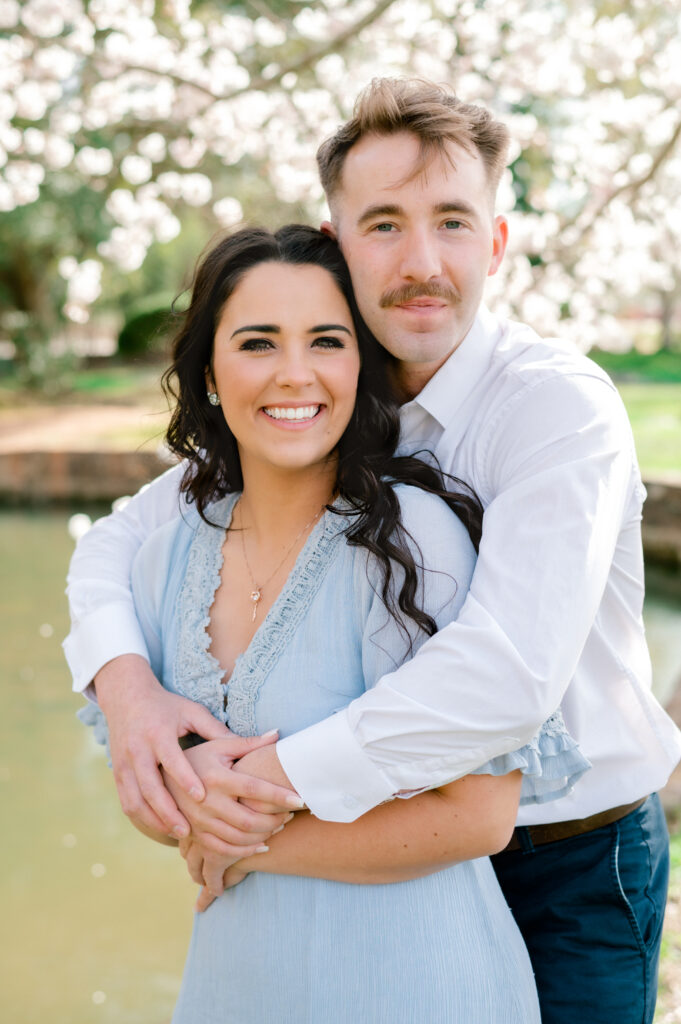 Couple standing in an embrace under cherry blossom trees beside the Asia pond at Furman University in Greenville SC