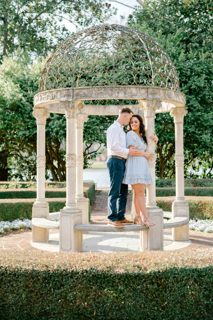 Man wearing white collared shirt nuzzling fiance's forehead at the Furman Rose Garden gazebo