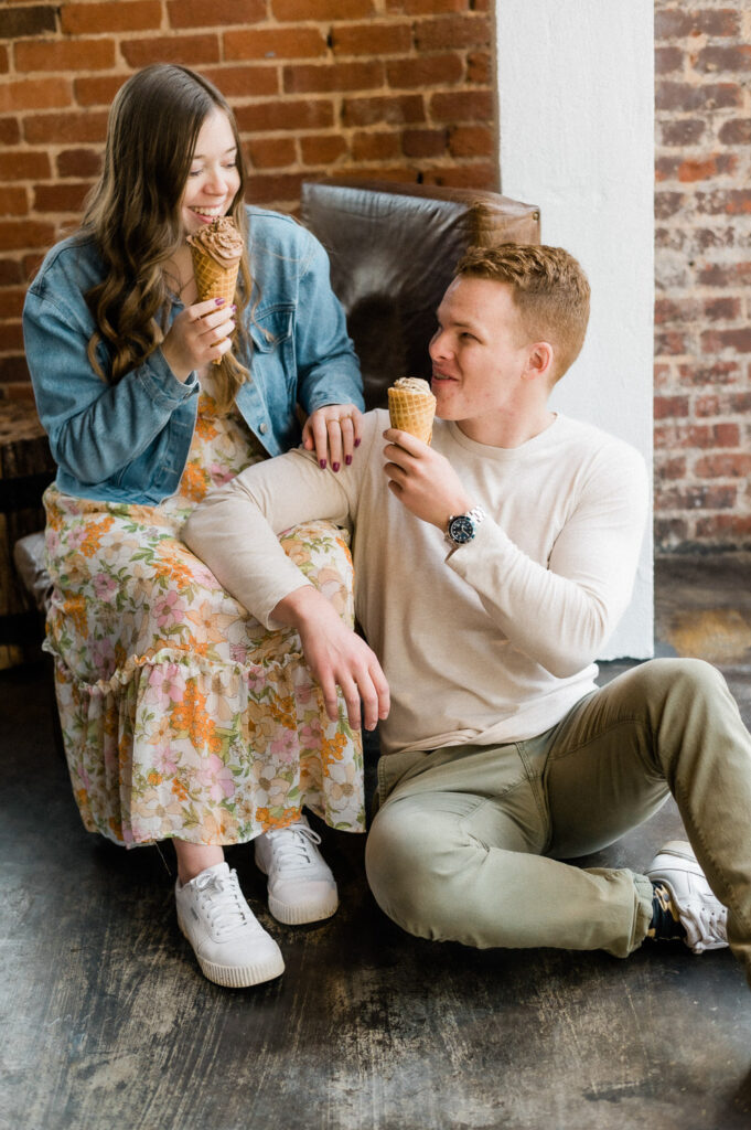 Smiling couple indoors enjoying ice cream cones by a brick wall