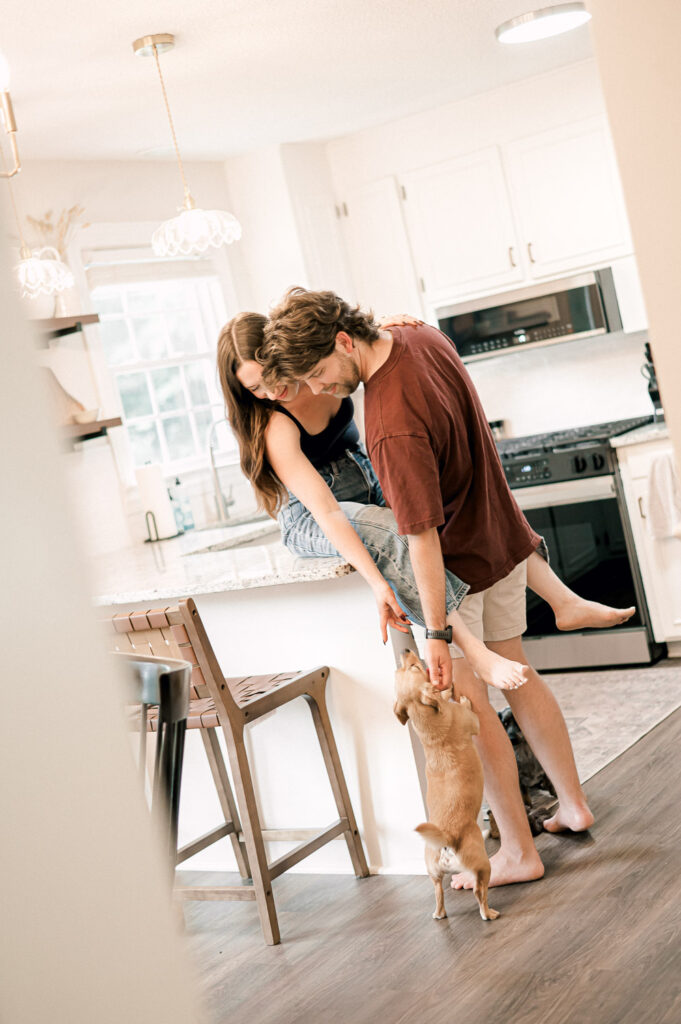 Couple laughing in a bright kitchen while playing with their dog in Greenville SC