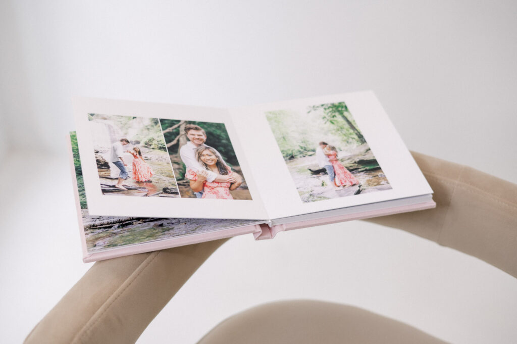 Open photo album on a chair displaying printed couples portraits and engagement photos in a bright, minimal room.
