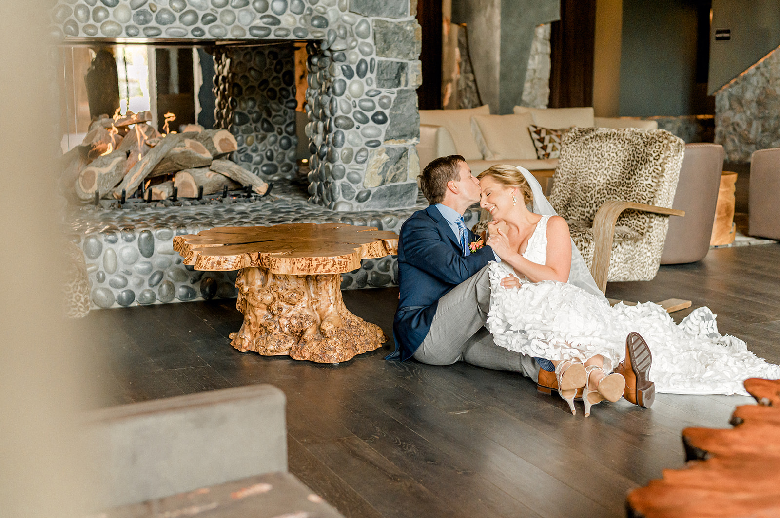 Newlyweds sit on the floor in front of a large stone fireplace snuggling and smiling before heading to romantic restaurants in Greenville, SC
