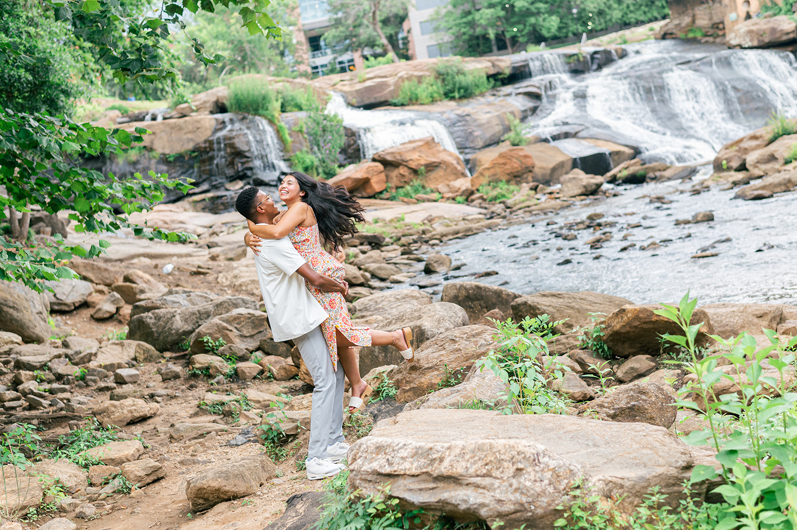 A happy couple sping and laugh by a beautiful waterfall in a colorful dress and white shirt